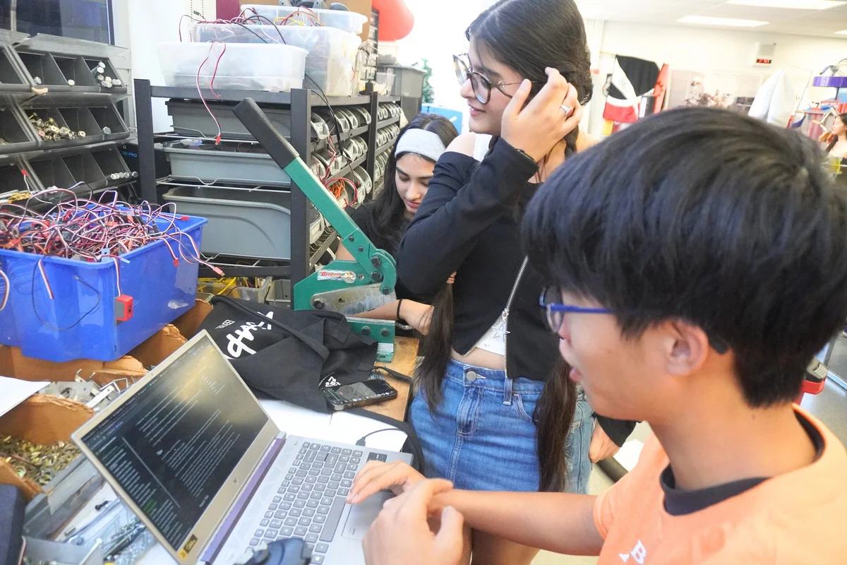 Students working at a laptop beside a robot and electronic components.
