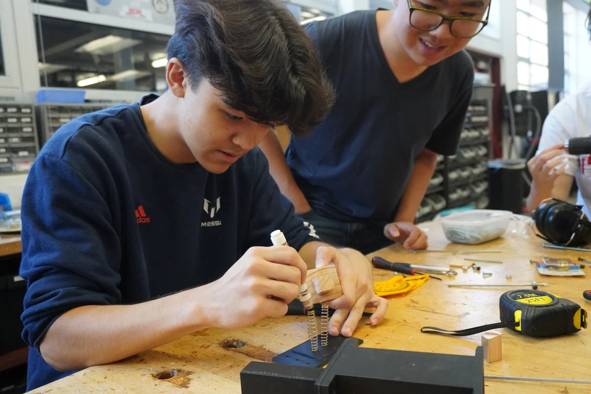 Two students assembling a small device at a workbench.