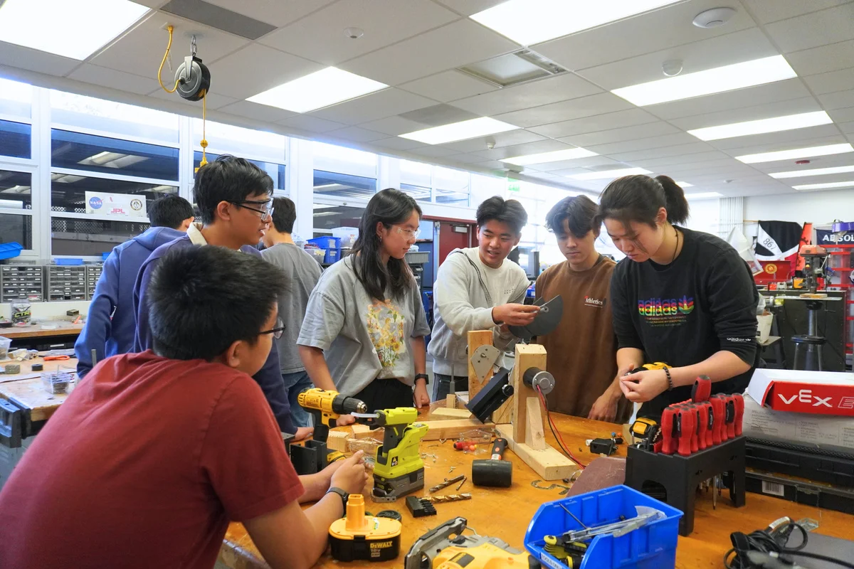 Team members gathered around tools and materials on a workshop table.